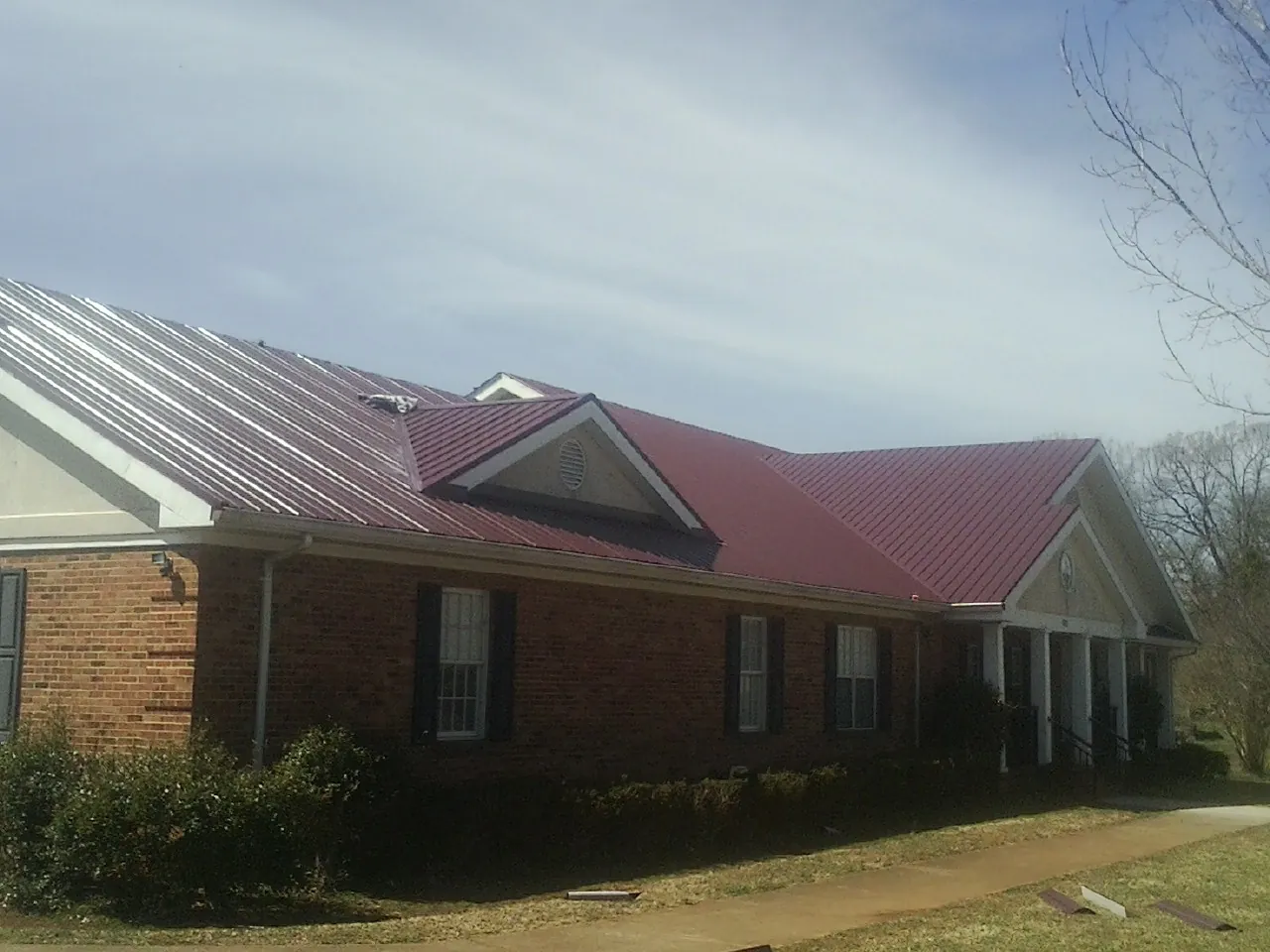 Red metal roof with gabled entries on a long brick building, from a Hail Damage Roof Repair job in Bemidji