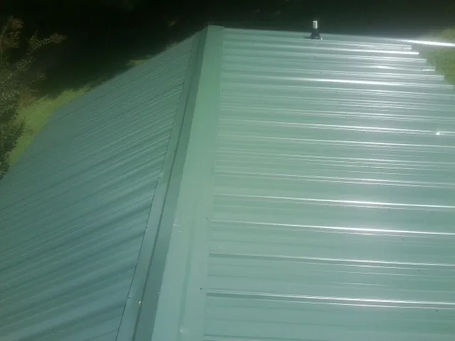 New green metal panels meeting at the ridge of a roof — Flat Roof Repair work by our crew in Bemidji