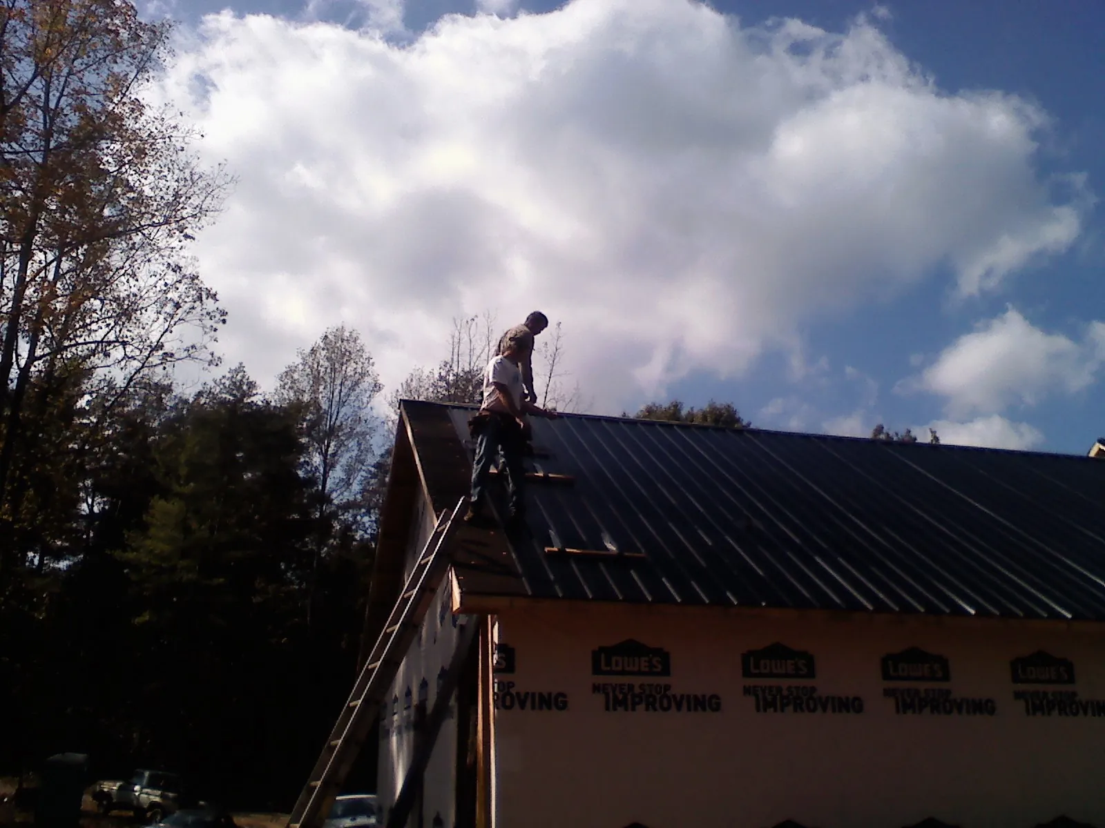 Roofer fastening dark metal panels high against a cloudy sky, from a Roof Inspection job in Bemidji