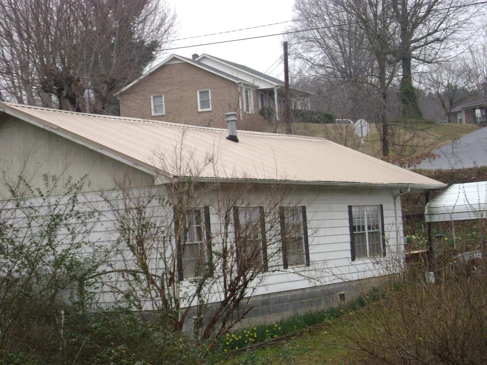 Tan metal roof on a white sided house set into a hillside — Commercial Roofing by Roofing Brothers in Bemidji