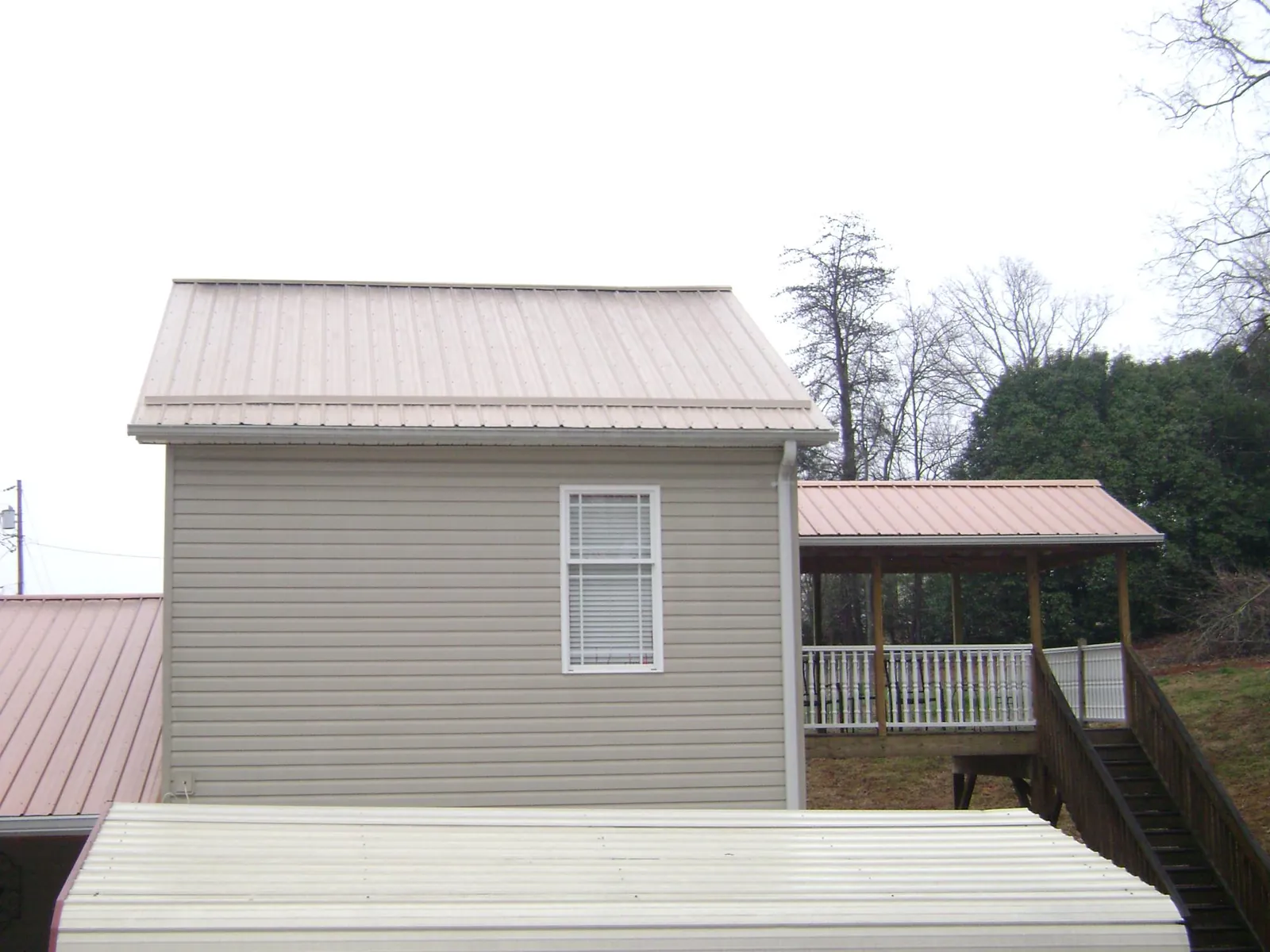 Tan metal roofs on a two story addition and attached porch, from a Roof Replacement job in Bemidji