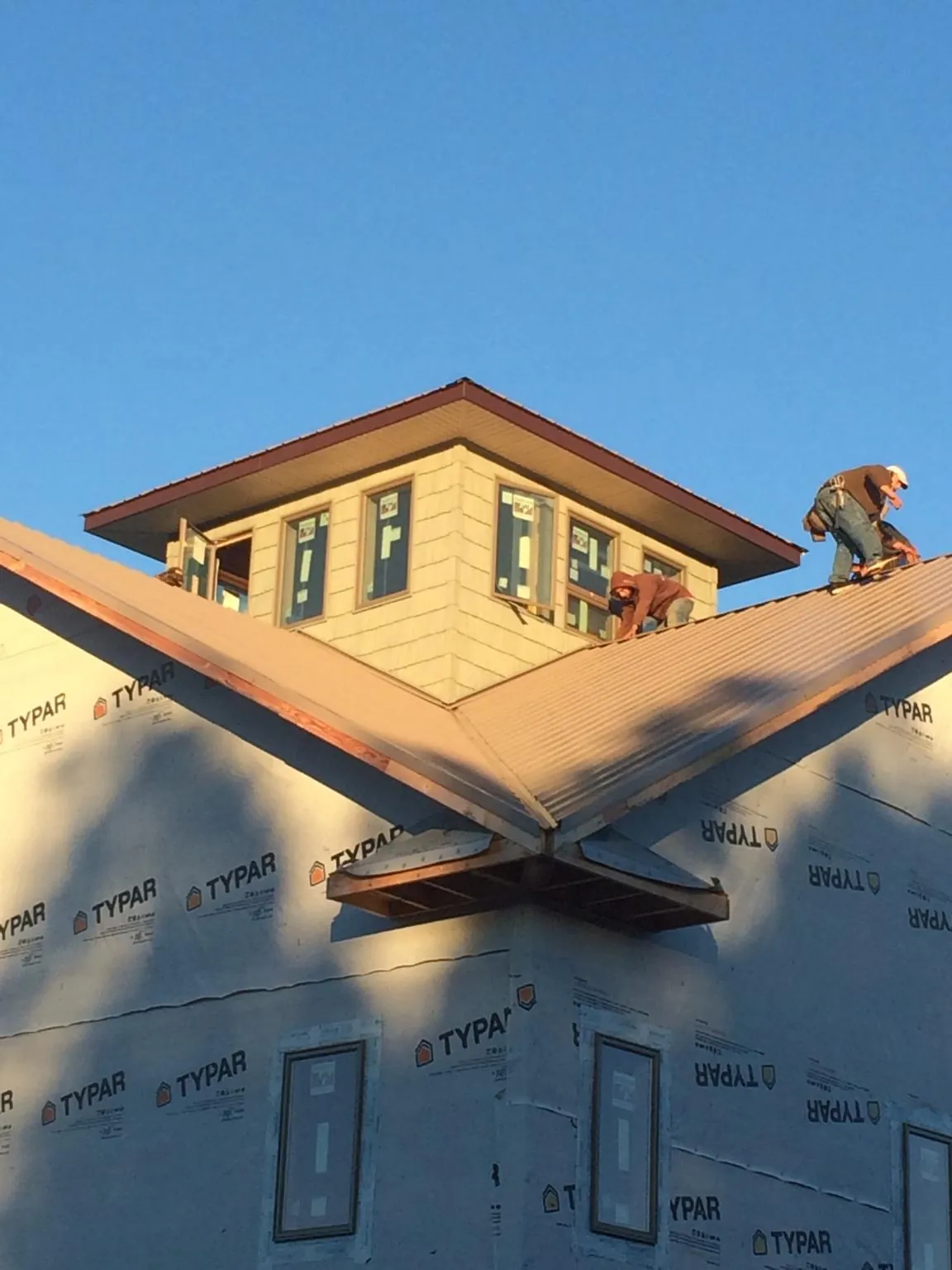 Roofers working around a rooftop cupola on a new metal roof at sunset — Roof Waterproofing in Bemidji by Roofing Brothers